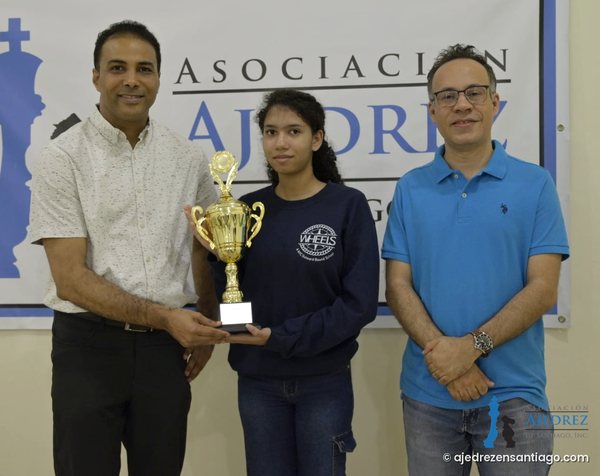 Esther Ramírez Beras recibe el trofeo de Campeona Nacional Juvenil Femenina 2026 de manos de Willy González, presidente de la Federación Dominicana de Ajedrez (FDA), junto a Leonardo Rafael Estévez, presidente de la Asociación de Ajedrez de Santiago (AAS)
