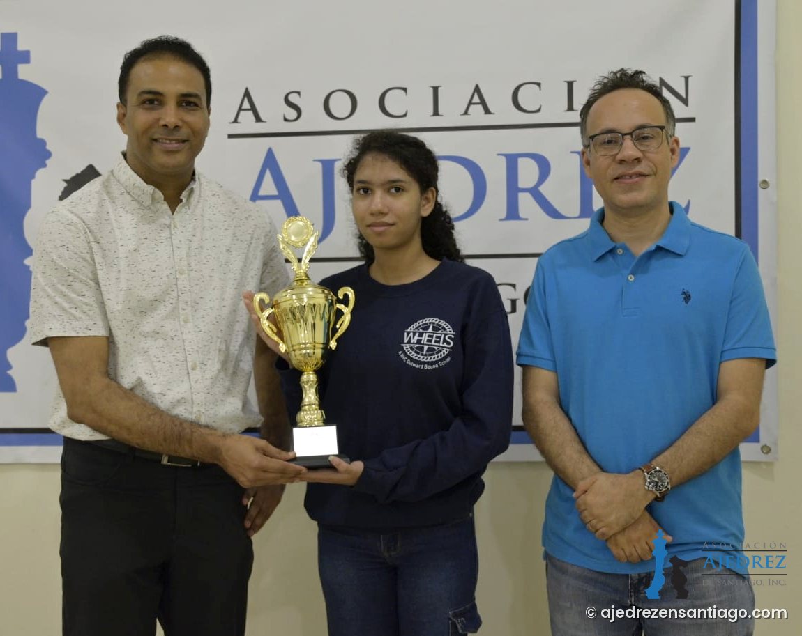 Esther Ramírez Beras recibe el trofeo de campeona de manos de Willy González, presidente de la Federación Dominicana de Ajedrez (FDA), junto a Leonardo Rafael Estévez, presidente de la Asociación de Ajedrez de Santiago (AAS)